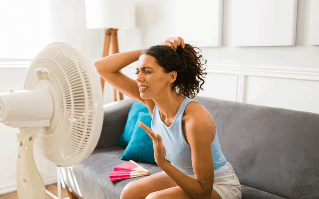 Femme épuisée assise devant un ventilateur dans son appartement pendant une vague de chaleur estivale - image symbolique de la hausse des températures en été 2025