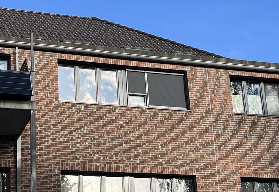 Façade en briques avec stores pare-soleil de CLIP'N'SHADE sur deux fenêtres de l'extérieur.